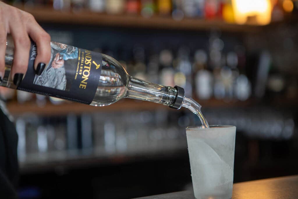 A bartender pouring Sandstone Distillery vodka over ice at the Quarry Bar, with the back bar out of focus behind