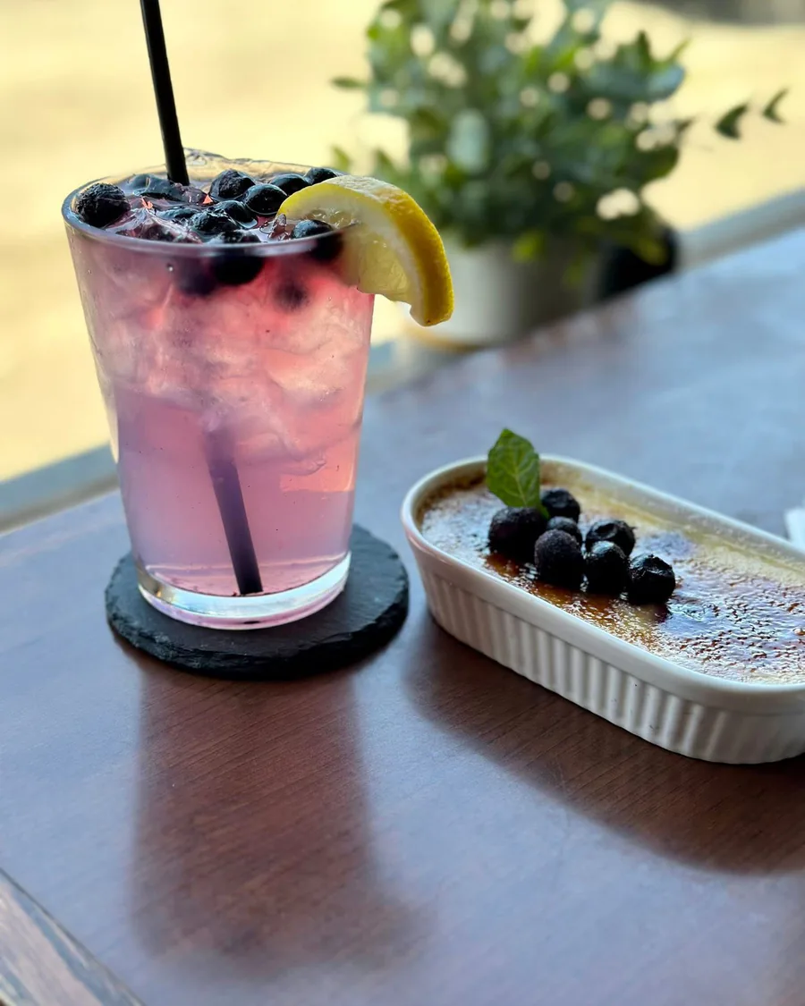 A blueberry and lemon cocktail beside a berry-topped dessert