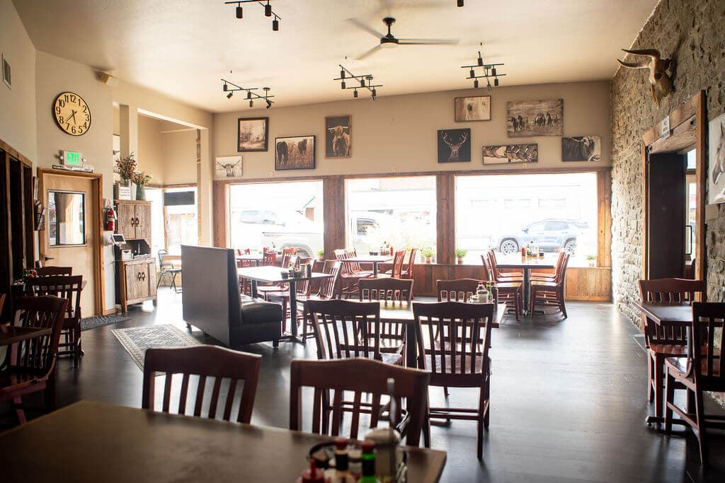 Wide view across the cafe dining room toward the storefront windows, with booths, track lighting, and western prints on the walls