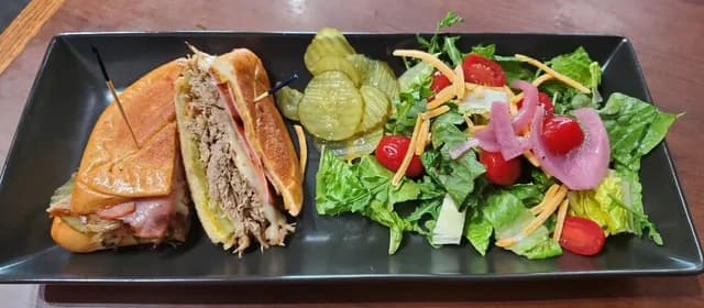 A toasted sandwich served with pickles and a garden salad