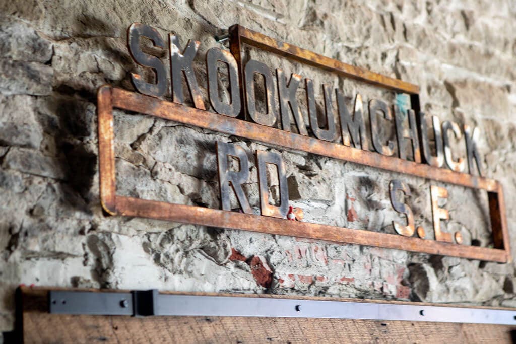 A salvaged Skookumchuck Rd S.E. street sign in weathered metal, mounted on the cafe's rough stone wall